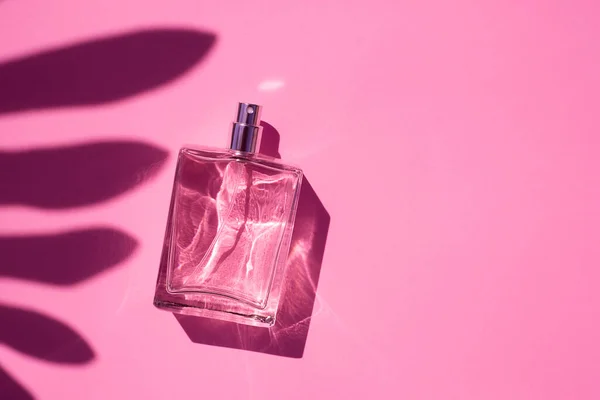 Transparent bottle of perfume on a pink background. Trending concept in natural materials with palm leaves shadow. — Stock Photo, Image