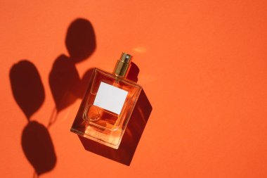 Turuncu arka planda saydam bir parfüm şişesi. Gün ışığıyla parfüm sunumu.