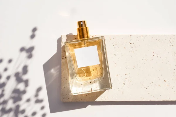 Frasco transparente de perfume con etiqueta blanca en placa de piedra sobre fondo blanco. — Foto de Stock