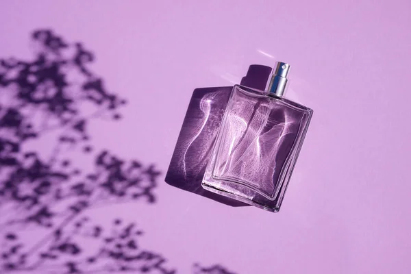 Transparante fles parfum op een lila ondergrond. Parfumpresentatie bij daglicht. — Stockfoto
