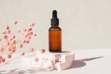 Podyumda siyah kapaklı kehribar cam damlası şişesi ve arka planda kuru bitkiler..