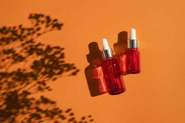 Turuncu arka planda gümüş kapaklı kırmızı cam damlalar. Güzel gün ışığında cilt bakımı ürünleri.