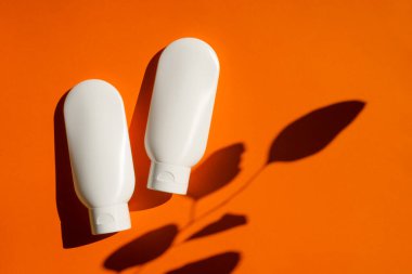 Turuncu arka planda krem ya da losyon için iki plastik beyaz tüp. Cilt kremi kozmetik.
