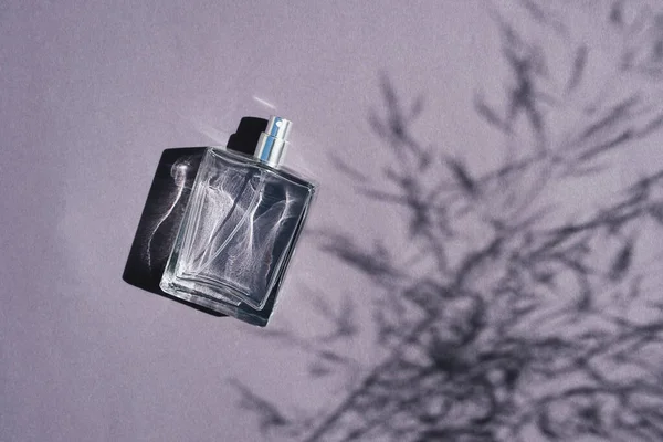 Frasco transparente de perfume sobre fundo lilás. Apresentação de fragrância com luz do dia. — Fotografia de Stock