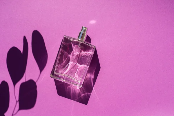 Frasco transparente de perfume sobre fondo púrpura. Presentación de fragancias con luz natural — Foto de Stock