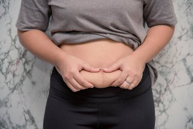 Beyaz arka planda karnına dokunan şişman bir kadın.