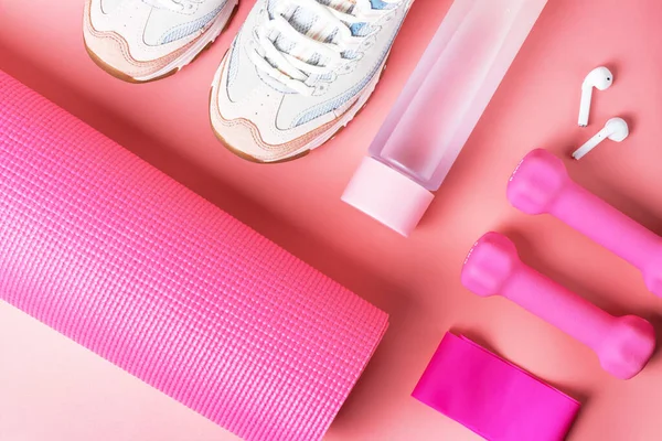Sports accessories and sneakers on a pink background, top view.