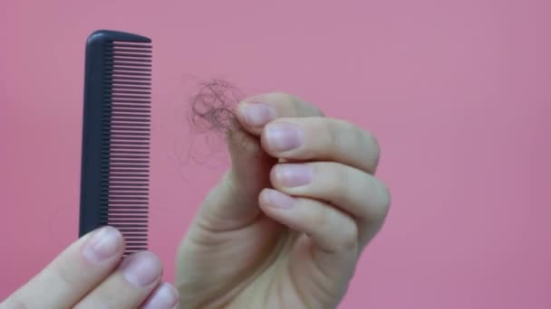 Female hands holding comb and falling hair on pink background. — Stock Video