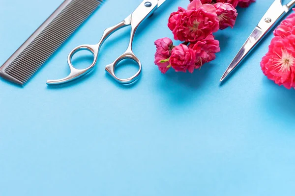Scissors, comb and flower on blue background with copy space.