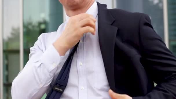 Man trekt jas aan tegen de achtergrond van een kantoorgebouw. — Stockvideo