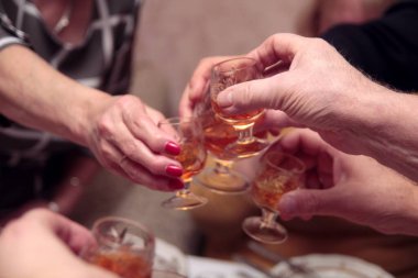 Birkaç yaşlı insanın konyak ya da konyakla doldurulmuş küçük kristal bardakları tıkırdattığı yakın plan bir fotoğraf. Aile toplantılarının, yıldönümlerinin ya da bayram kutlamalarının sıcak, şenlikli atmosferi. Gözlüklere odaklan..