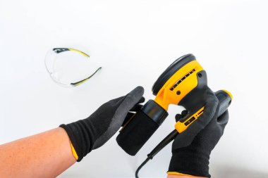 Dairesel elektrik zımpara makinesi, öğütücü alet, güçlü erkek ellerinde toz toplamak için kabı olan yüzey zımparalama makinesi, beyaz arka planda bulanık koruyucu gözlük, yatay pankart, kopyalama alanı.
