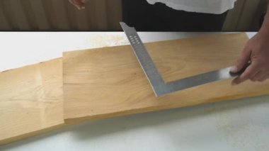 Bronzlaşmış erkek marangozun ellerini kalem ve inşaat karesiyle testereyi çizerek tahta bölmeyi işaretleyen beyaz boyalı tezgahı kapat. Kendin yap, ev işi, yüz yok.