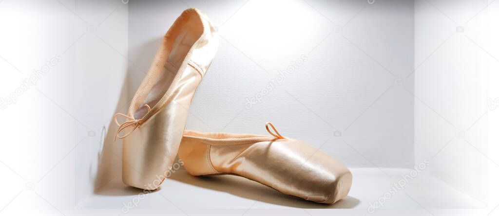 Close-up new beige pink ballerina pointe shoes in concrete wall niche,light background,side view,copy space.Dance training accessories shop.Classical ballet school concept.Education in field of arts.