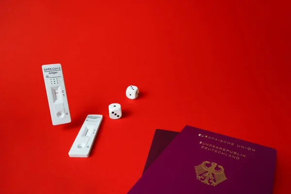 Rapid SARS-Cov-2 Antigen test,negative result,unused,dice on red,pair of german tourist passport.Bad or good luck concept for european traveller crossing border,quarantine.Play fate game,copy space.