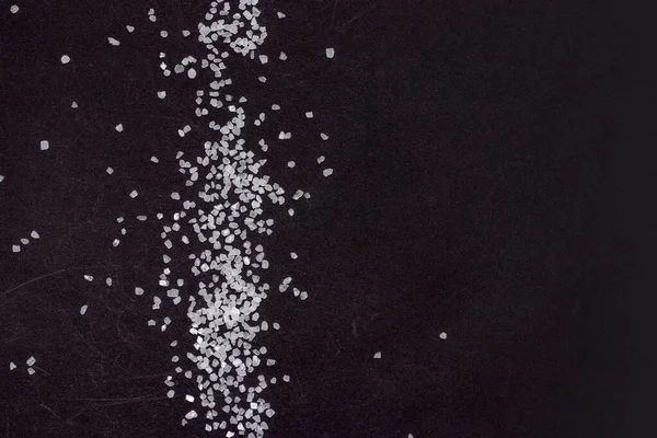 Spilled white sea salt on a black background. clear crystalline pebbles on a black background.