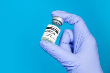 Aşı Coronavirus COVID-19. Mavi arka plandaki doktorun elindeki cam şişede Coronavirus aşısı. Aşı Coronavirus 'a karşı savaş kavramı