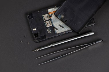 Bozuk cep telefonu ve tamir araçları koyu arka planda, düz yatıyordu