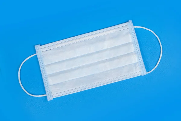 Surgical mask with rubber ear straps. Typical 3-ply surgical mask to cover the mouth and nose. Procedure mask from bacteria. Protection concept. Blue background.