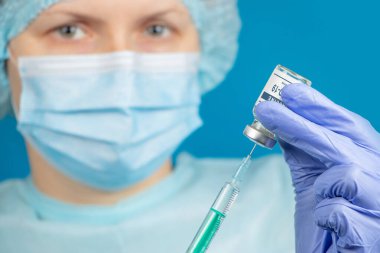 Coronavirus COVID-19 'a karşı aşı. Bir doktor mavi arka plandaki cam bir şişenin içindeki şnitzle koronavirüse karşı aşı yazıyor. Coronavirus aşısı konsepti.