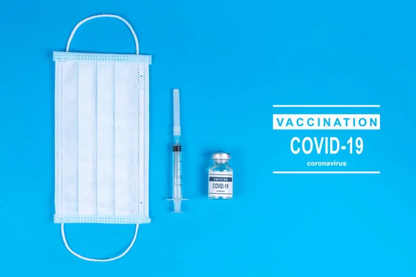 Medical bottle, vials, syringes and face mask on blue background with copy space. Vaccination session and immunity improvement