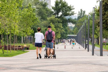 Parkta bebek arabasında yürüyen bir çift ve bir kadın.