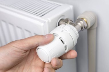 Bir adamın eli radyatör termostatının ısısını ayarlar.,