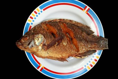 Tabakta kızartılmış tilapia var. Siyah bir arkaplanda.