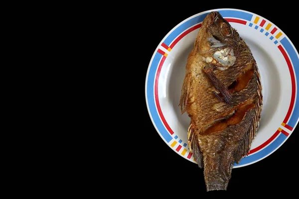 Tabakta kızartılmış tilapia var. Siyah bir arka planda. Metni yerleştirmek için boş bir alan var.