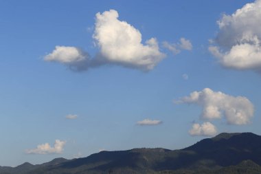 Gökyüzü filler, ayılar, kuşlar gibi hayvan şeklinde bulutlarla kaplı. Dipte bir sıra dağ var..