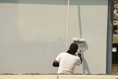 Bir erkek işçi iple yüksek bir binayı boyuyor..