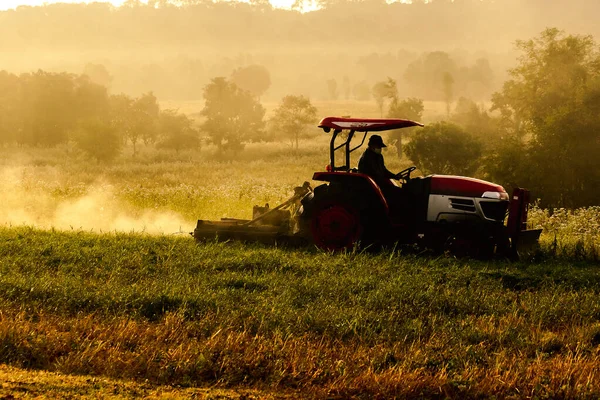 A man driving a lawn mower, a tractor working on the land.
