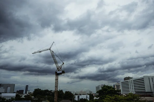 A tall crane operates in thunderstorm weather before it rains.