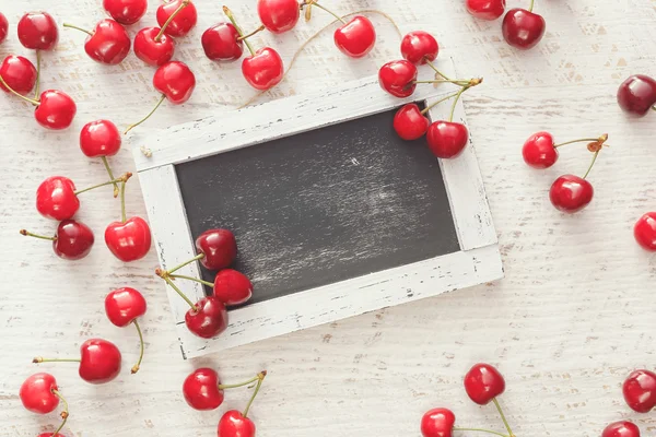 Cerejas em torno de chalkboard vazio — Fotografia de Stock