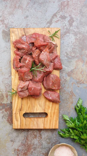 Carne crua em cubos com um ramo de alecrim — Fotografia de Stock