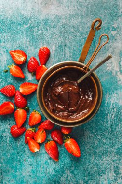 Bakır kapta erimiş çikolata ve yanında çilek parçaları. Üst görünüm, boş boşluk