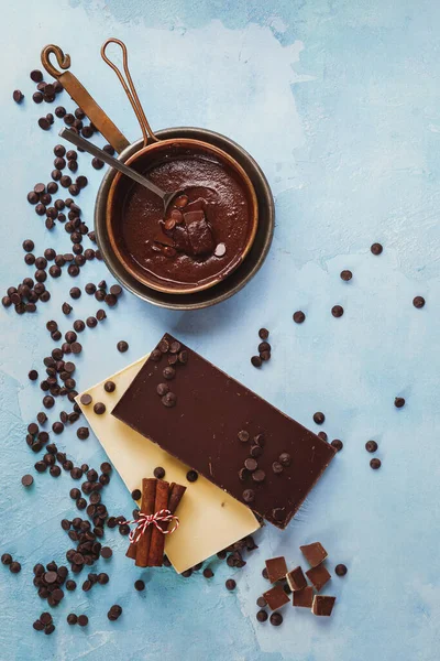 A bars of dark and white chocolate and melted chocolate in copper pan on rustic blue surface. Top view, blank space