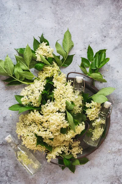 Metal bir tepside taze yaşlı çiçekler. Gri arka plandaki eski bir şişede likörle birlikte. Üst görünüm, boş boşluk