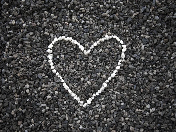 El corazón de pequeñas piedras blancas en la superficie de las piedras oscuras Imagen de stock