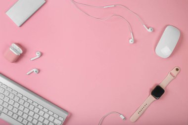 Ofis eşyalarının arka planında pembe arka plandaki akıllı cihazların bir kopyası. Bilgisayar faresi ve klavye, kulaklıklar, akıllı saat ve güç bankası. Fotokopi alanı olan üst görünüm, düz. Kadın aygıtları