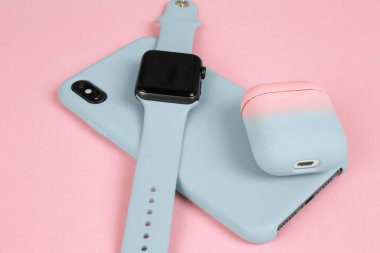 Telefon, akıllı saat ve pembe arka planda şık mavi çantalarda kablosuz kulaklık.