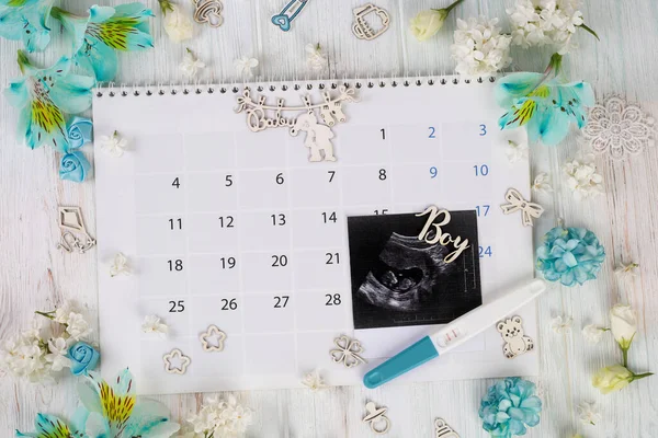 Baby ultrasound and pregnancy test on calendar background. This is a boy! Child planning. Pregnancy concept.