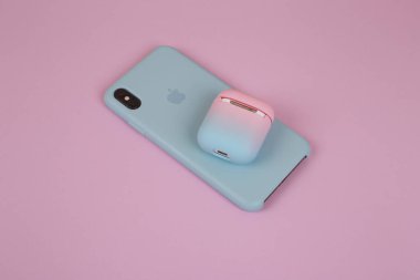 Silikon çantalı bir telefon ve eflatun arkaplanlı bir kulaklık kutusu. Şık bir telefon ve kulaklık. Kadın aygıtları