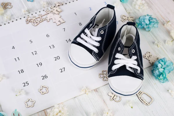 Baby first sneakers on calendar background. Little baby shoes. Child planning. Pregnancy concept. Baby boy first steps.