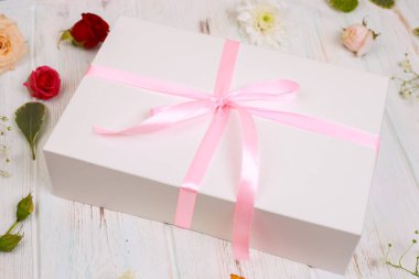 Çiçeklerle birlikte pembe kurdeleli bir hediye. Kutlama