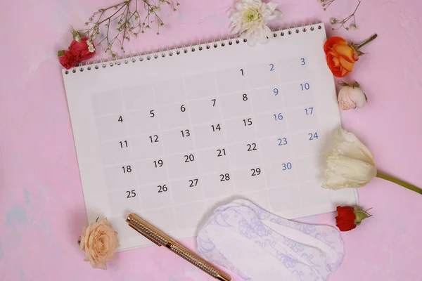 Menstrual cycle calendar on calendar background. Pink floral background with pads. Ovulation concept. Menstruation concept. Woman red calendar.