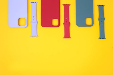 Renkli silikon telefon kılıfları, saat kayışı ile birlikte. Hazır ol. Güncel teknoloji. Sarı arka planda duran çeşitli kişisel aksesuarların düz uzantısı. Metin için boşluk