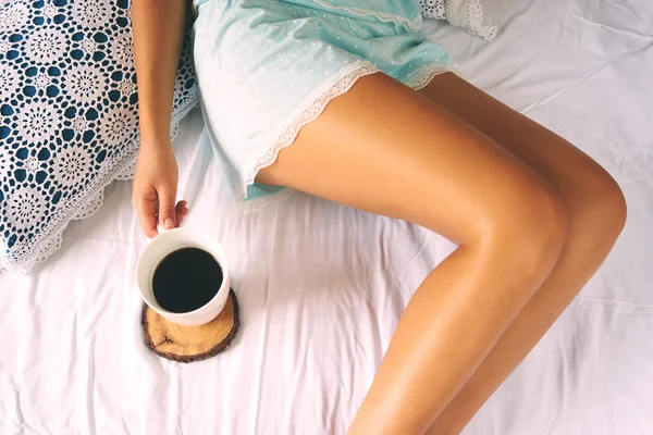 Jovem mulher desfrutando de seu café enquanto se senta na cama . — Fotografia de Stock