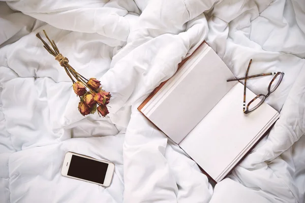 Dry roses, smartphone and vintage notebook on bed — Stock Photo, Image