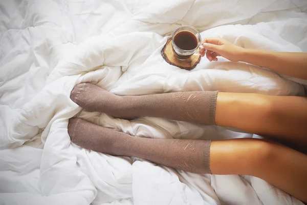 Mujer joven disfrutando de su café mientras está sentada en la cama . —  Fotos de Stock